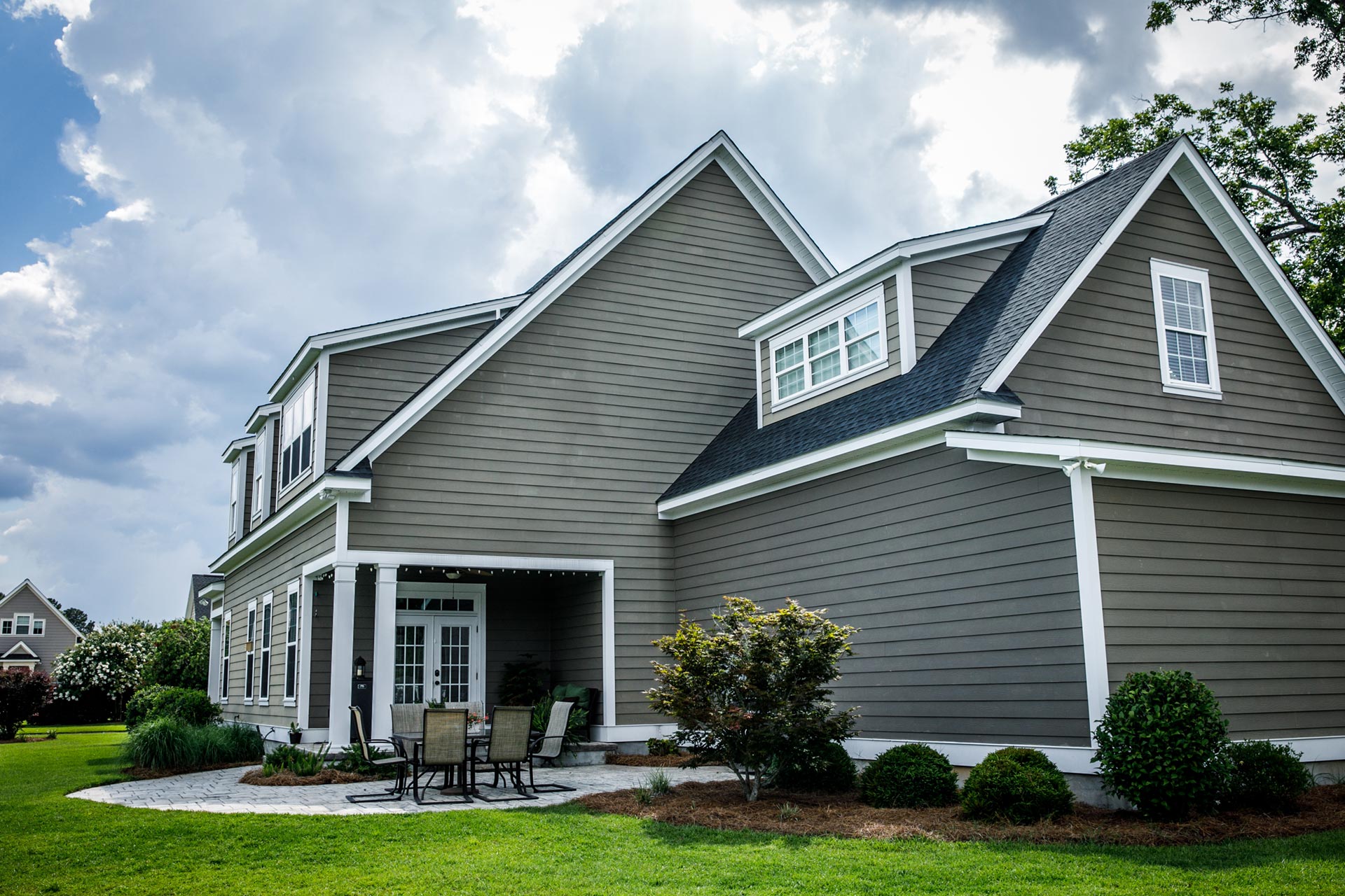 Newly installed siding and gutters on residential home featuring gray stone veneer and dark vertical metal siding by WMT Siding and Gutters.